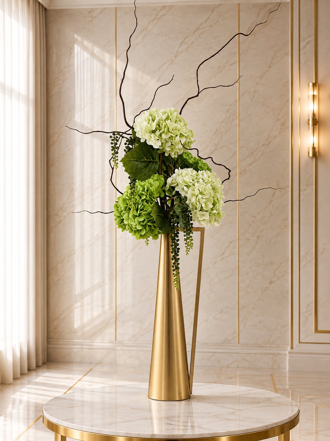 A Petal & Pearl table rental: green and white silk hydrangeas with curly willow in a tall brushed-gold vase on a marble table